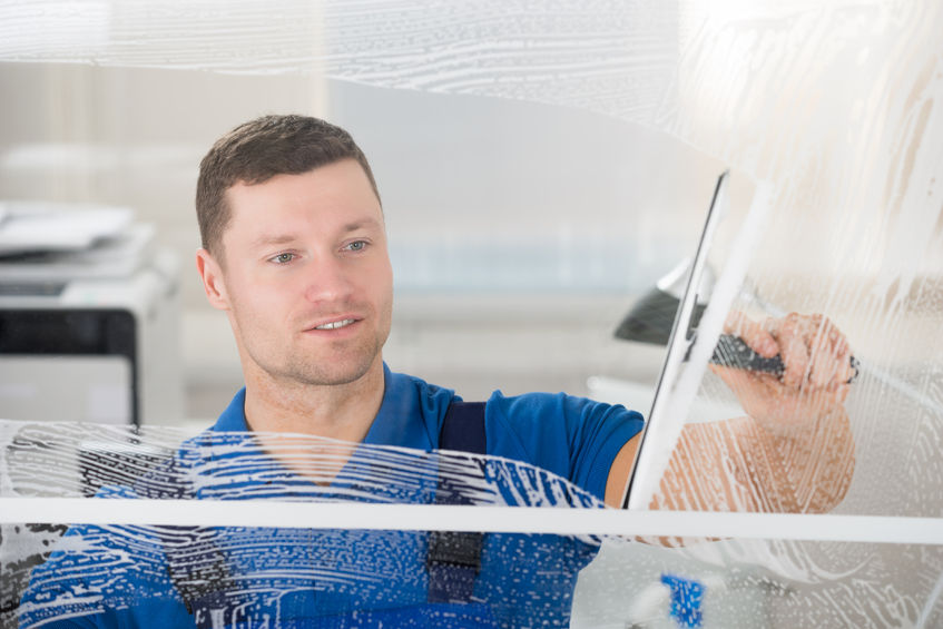 50691542 - smiling mid adult worker cleaning soap sud on glass window with squeegee