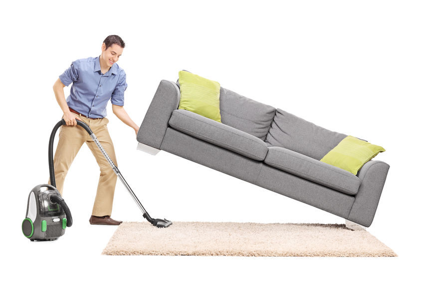 38831697 - cheerful young man lifting a sofa and cleaning underneath it with vacuum cleaner isolated on white background